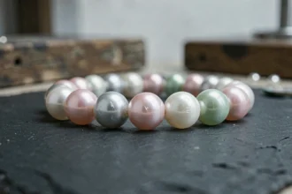 Gros plan sur un collier de perles de culture aux reflets variés posé sur ardoise, révélant les différences de nacre et de qualité